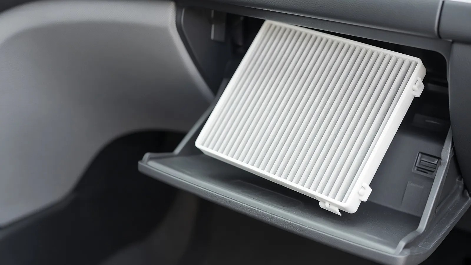 White pleated cabin air filter sliding into the open filter slot behind a car glove box