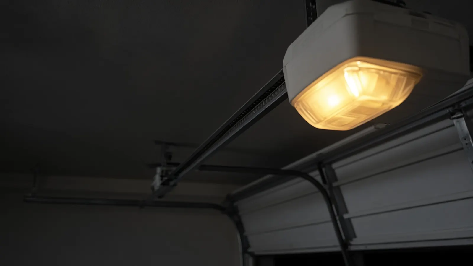 Ceiling-mounted garage door opener with its light glowing above a half-open door and rail
